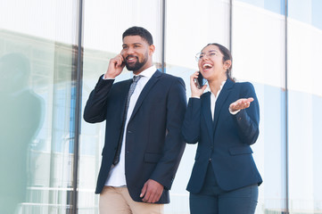 Fototapeta premium Happy excited business colleagues enjoying funny phone talks outdoors. Smiling man and woman in office suits speaking on cells and getting good news. Success and communication concept