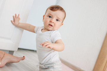 Fototapeta premium Charming little boy 6-8 months looking at the camera on the background of mom's feet