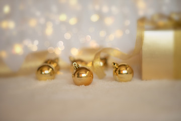 Gold Christmas background of defocused twinkling lights with gold balls, decoration and gift box. Selecnive focus. Toned image with copy space for your text.