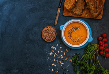 Bowl of pumpkin organic soup with cream and pumpkin seeds on gray background. Dietary vegetarian food. Concept of healthy eating food. Homemade autumn soup. Top view with copy space. Toned image.