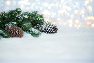 Fototapeta na wymiar Blurred christmas tree branches, snow and pine cones with twinkling lights. Holiday mock up. Toned image with copy space. Selective focus.