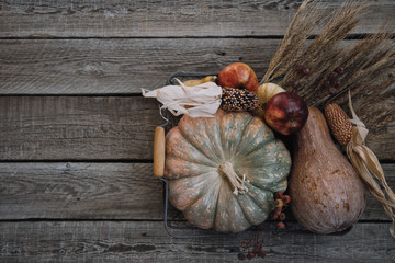Thanksgiving background. Pumpkins, apples, leaves, ears of wheat and spices on brown wooden background. Seasonal fall background for Thanksgiving or Halloween. Design mock up. Horizontal, toned image.