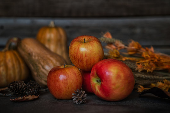 Ripe red apples with pumpkins in the background. Autumn background from yellow flowers, fruit and vegetables. Fall season, eco food and harvest concept. Selective focus. Toned image.
