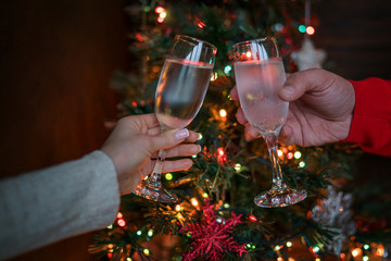 Two glasses of champagne raised in a toast against a Christmas tree glowing lights. Holiday and togetherness a family Christmas and Happy New Year. Party time. Couple with champagne. Selective focus.