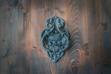 Old metal door handle knocker on a rough wooden background. Ancient door patina dark blue metal knocker of old family house. Vignette wood door background