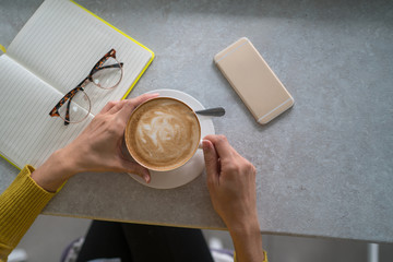 Female hands holding cup of coffee on table background. Coffee cup in coffee shop. Closeup image woman drinking hot coffee in cafe. Vintage style effect picture. Selective focus.