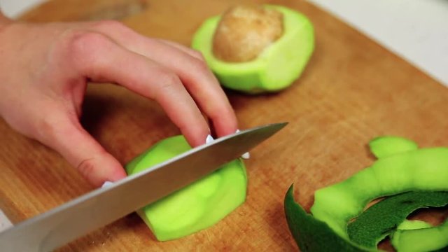 Close-up of female hands breaking and cutting a peeled avocado on the wooden cutting board