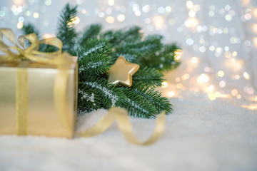 Gold Christmas background of defocused lights with fir branches, decoration and gift box. Selecnive focus. Toned image with copy space for your text.