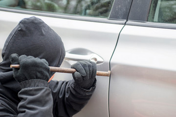 Male thief going to break car window with crowbar. Car theft - thief trying to break into the...