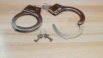 Handcuffs and key on light wooden background. Security, crime and punishment concept.