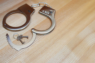 Handcuffs and key on light wooden background. Security, crime and punishment concept.