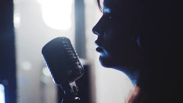 Close-up profile of attractive female musician singing a song in recording studio
