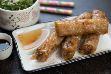 Close-up of deep fried vietnamese spring rolls with dipping sauces and seaweed salad, selective focus