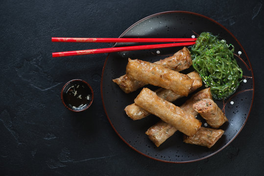 Vietnamese nems or deep fried spring rolls with pork meat, flatlay over black stone background, horizontal shot