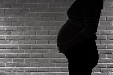 Backlight of a pregnant woman. Silhouette of young pregnant female on brick wall background. Backlit silhouette.