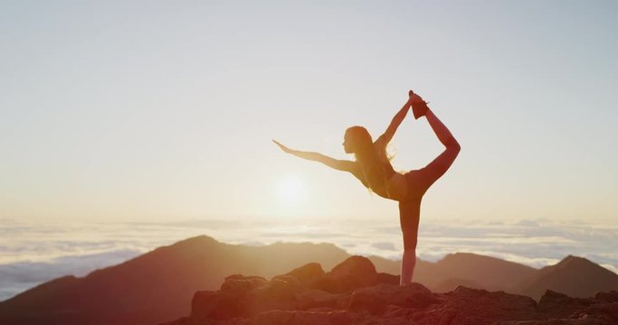 Young athletic woman performing yoga pose on the top of a mountain at sunrise, zen wellness woman performs dancer's pose