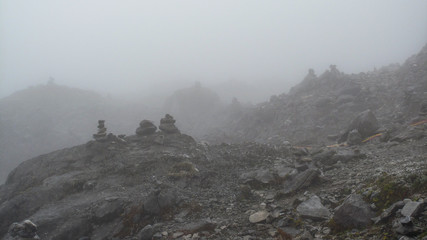Stacks of stone on a foot of stone mountain, mostly covered by fog. © Kamonchanok