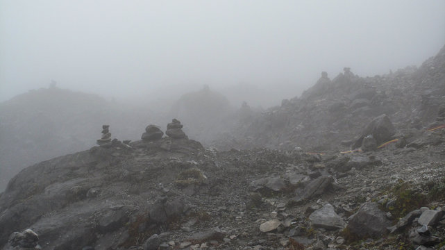 Stacks of stone on a foot of stone mountain, mostly covered by fog.