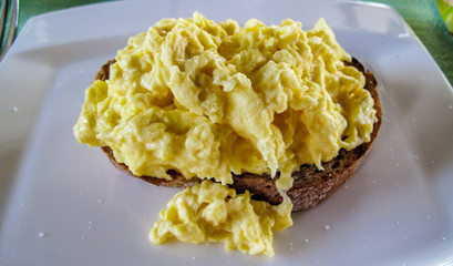 Scrambled eggs, a dish made from eggs stirred or beaten together in a pan while being gently heated, typically with salt, butter and various other ingredients. Top on toast in white dish. Close up.