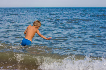The boy is swimming in the sea without hiding joy.