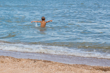 The boy is swimming in the sea without hiding joy.