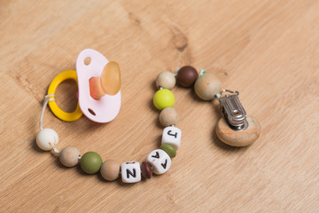 Pink pacifier with handmade playful chain with the baby name on a wooden surface