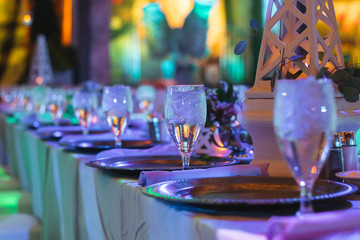 Elegant Plates and Crystal Wine Glasses set at Long Tables during an Event with Purple lighting