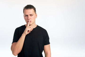 Young attractive man holding index finger near the lips on a white background.