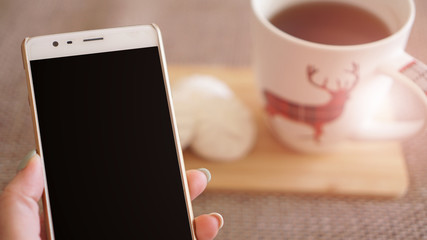 Woman uses white smart phone, womens hands, white background with copy space. Cup of black tea with white marshmallow. A warm atmosphere