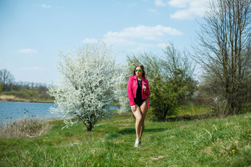 Girl in a black bodysuit and a pink jacket in nature with a flowering tree