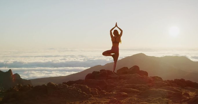 Young athletic woman performing a yoga pose at sunrise on the top of a mountain, woman performing a tree pose