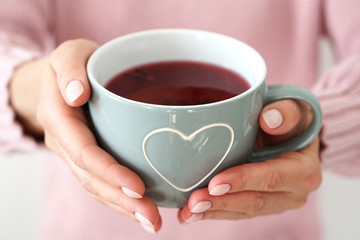 Woman s hands holding big mug with heart .