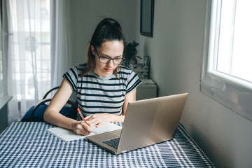 A young beautiful student girl does homework or writes a to-do list or this girl works in a home office. Home education or business or planning.