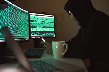 Computer security. Young man in black hoodie using multiple computers and his smartphone for...