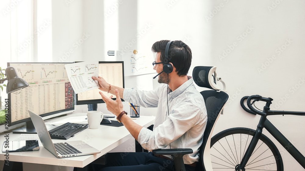 Poster growing chart. side view of happy young bearded trader in headset holding financial report, talking 