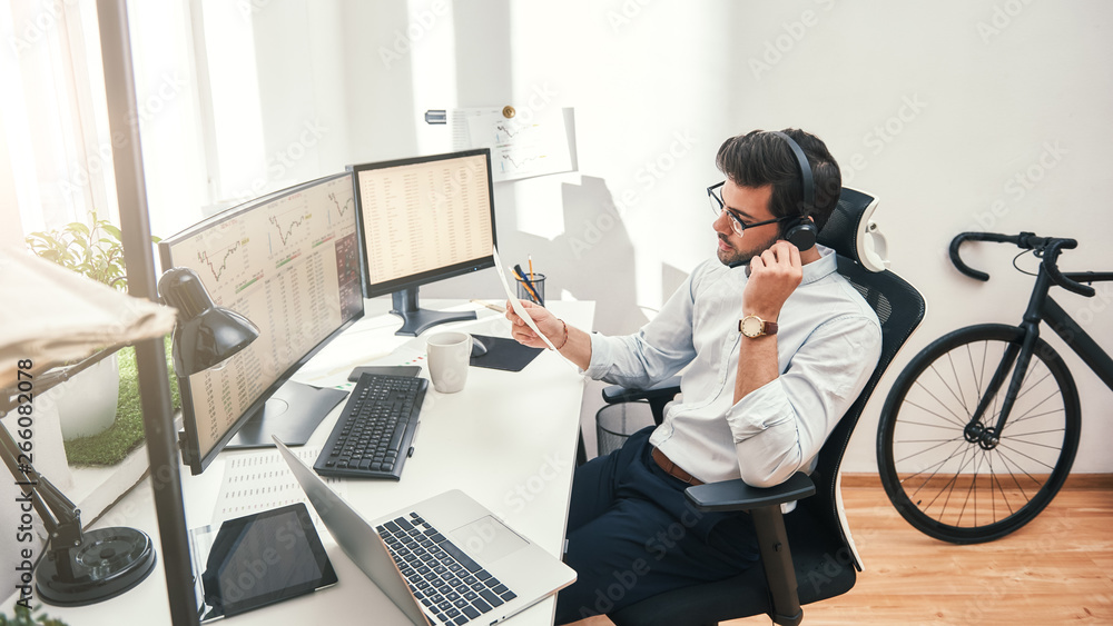 Poster talking about business. side view of young bearded trader in headset holding financial report and ta