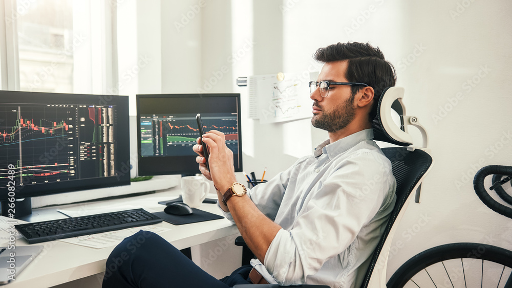 Aufkleber trading online. back view of young bearded trader in formal wear and eyeglasses using his smartphone