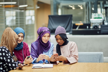Arabian young fashionably dressed in muslim clothes women watching on cellphone musical video clip standing together at shopping mall- Millennials, generation z and technology concept