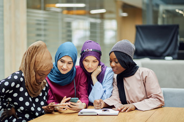 Islamic female travel blogger sharing info from smartphone with her followers while sitting in group of four in hotel lobby