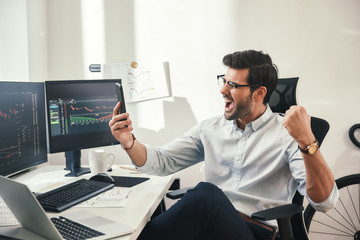Great! Excited young trader or businessman in formalwear and eyeglasses shouting and gesturing in...