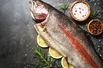 Raw salmon fish whole with ingredients for cookings on black.