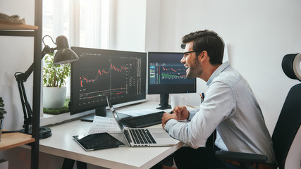 Great! Happy young businessman or trader in formalwear looking at charts on computer screen in the...