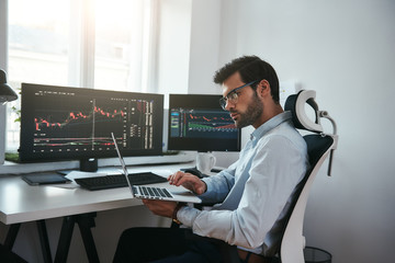 Business Information. Bearded trader wearing eyeglasses analyzing financial market via laptop while...