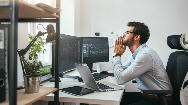 Important moment. Worried young businessman or trader in formalwear keeping palms together and looking at trading charts and financial data while working in the office.