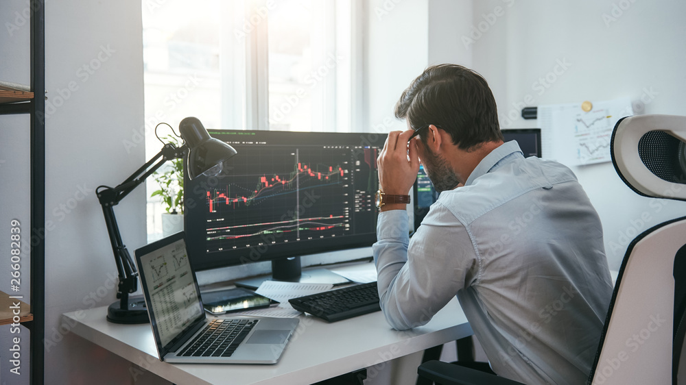 Fototapete working process. smart male trader looking at charts on multiple computer screens and analyzing data