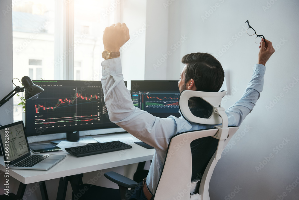 Fototapete yes! back view of stock trader with raised hands looking at multiple computer screens with data and 