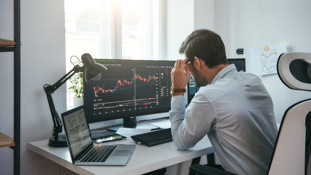 Working Process. Smart Male Trader Looking At Charts On Multiple Computer Screens And Analyzing Data While Sitting In His Modern Office