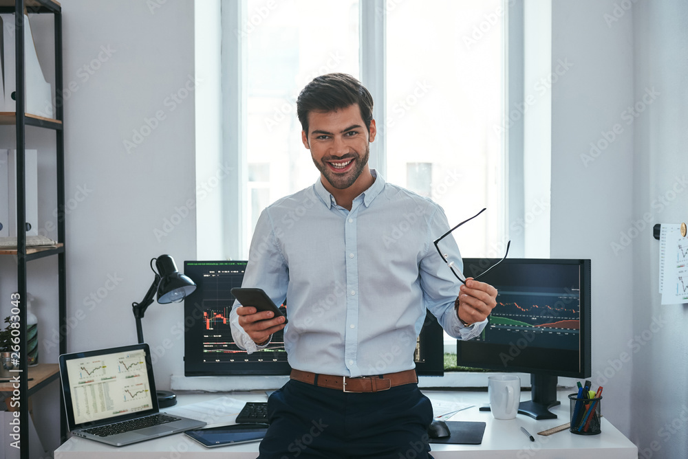 Aufkleber great! happy young businessman or trader in formalwear holding eyeglasses and smartphone and smiling