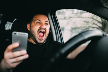 Young man sitting in his car screaming distracted by smartphone