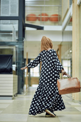 Smiling young islamic African woman wearing fashionable headscarf and dress standing on a metro train station with a bag in her hand